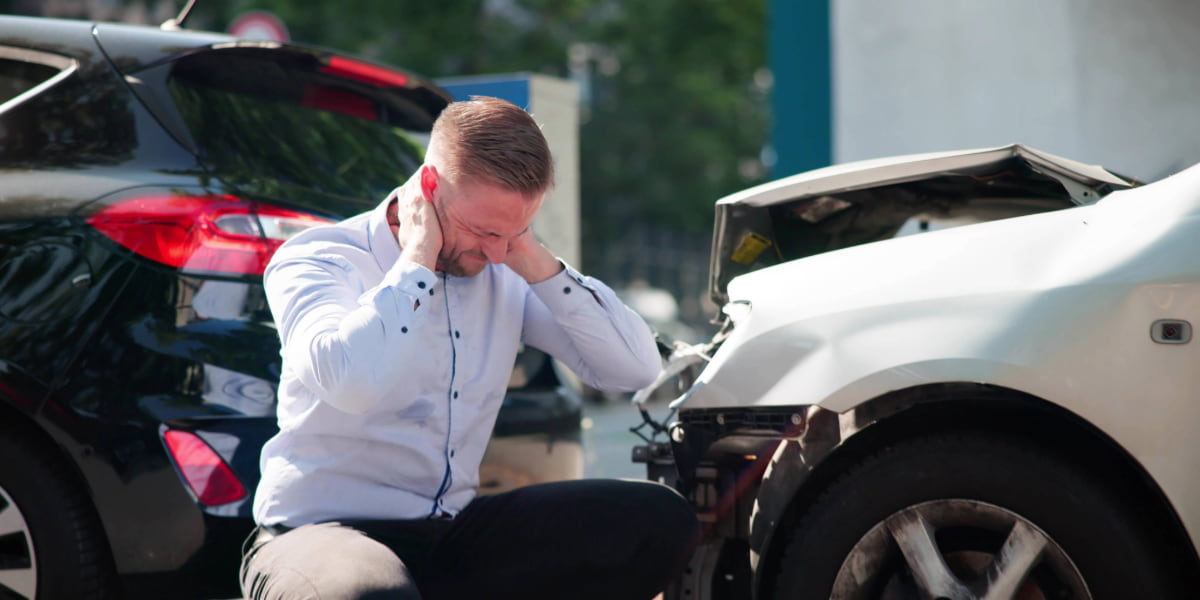 Man holding his neck beside two damaged cars showing car accident injuries and the immediate pain after a crash