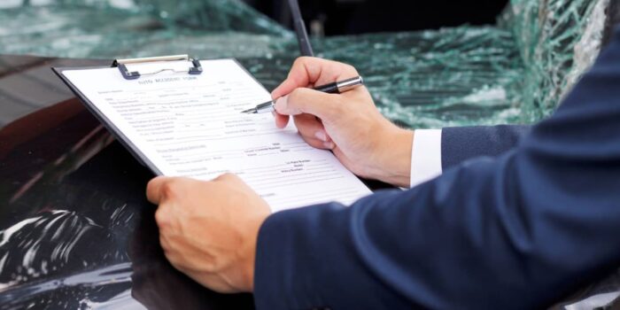 Person filling out an auto accident form beside a damaged vehicle for car accident settlement examples showing documentation after a crash