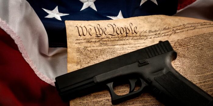 A handgun resting on the U.S. Constitution with the American flag in the background, symbolizing constitutional rights and florida gun laws.