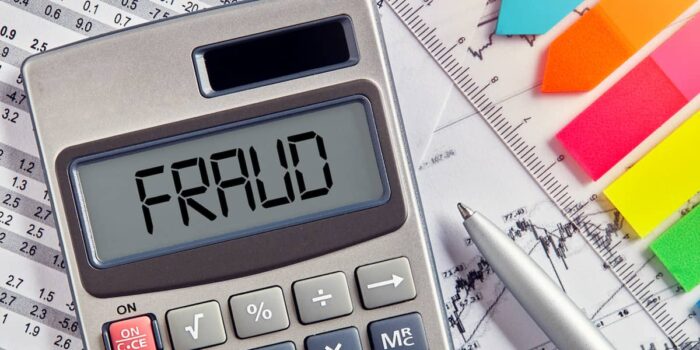 Calculator displaying "FRAUD" surrounded by financial documents and colored sticky notes, illustrating various types of fraud in business