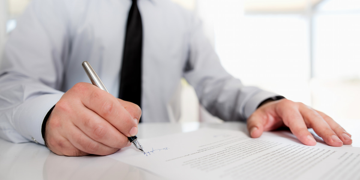 A person in a business suit signing legal documents at a desk, symbolizing legal actions and paperwork related to how to sue an insurance company.