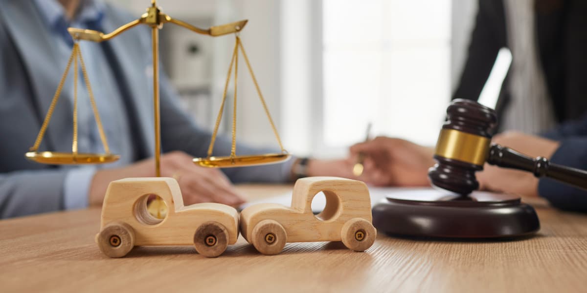 Scales of justice, wooden toy cars and a gavel on a desk showing what does a car accident lawyer do during a claim process