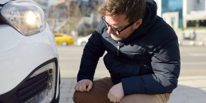 A man closely inspecting the front bumper of a white car after a minor accident, illustrating concerns about what happens if you crash a rental car.